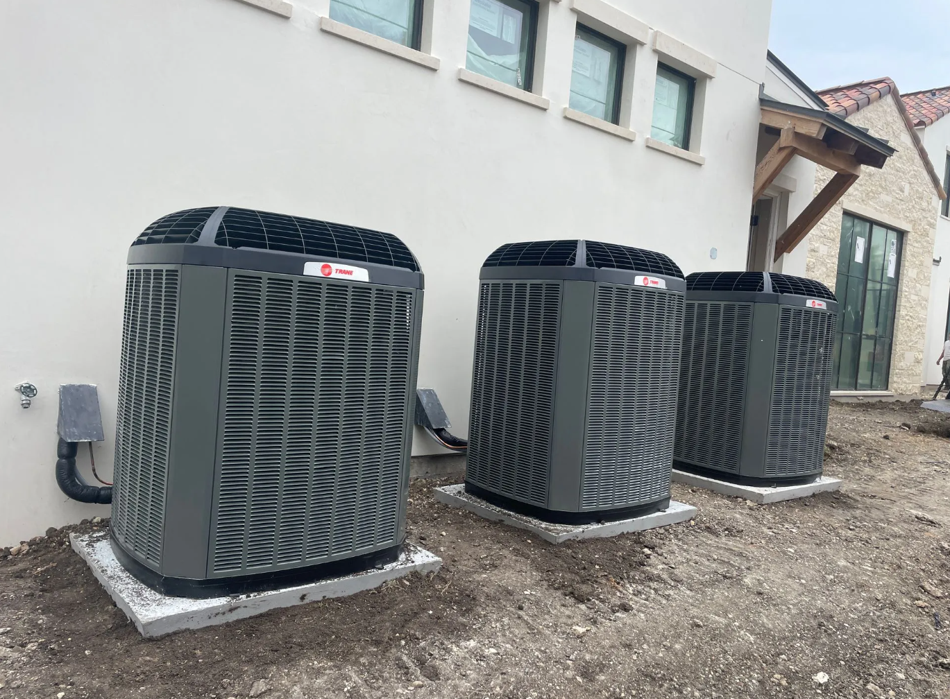 Three Trane condenser units lined up at a stone-and-stucco home
